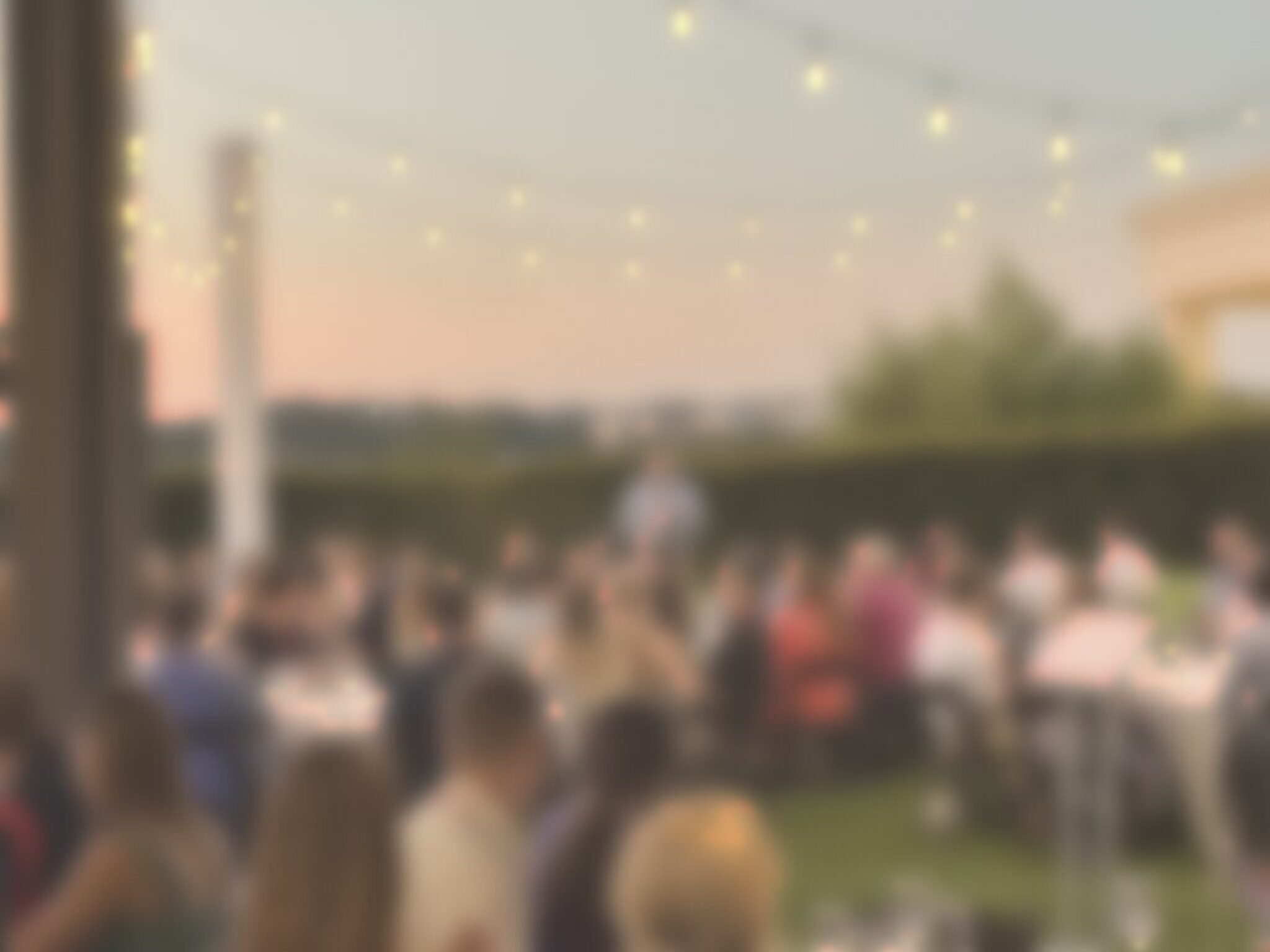 A full lawn dinner at sunset, softly blurred so no one is recognizable